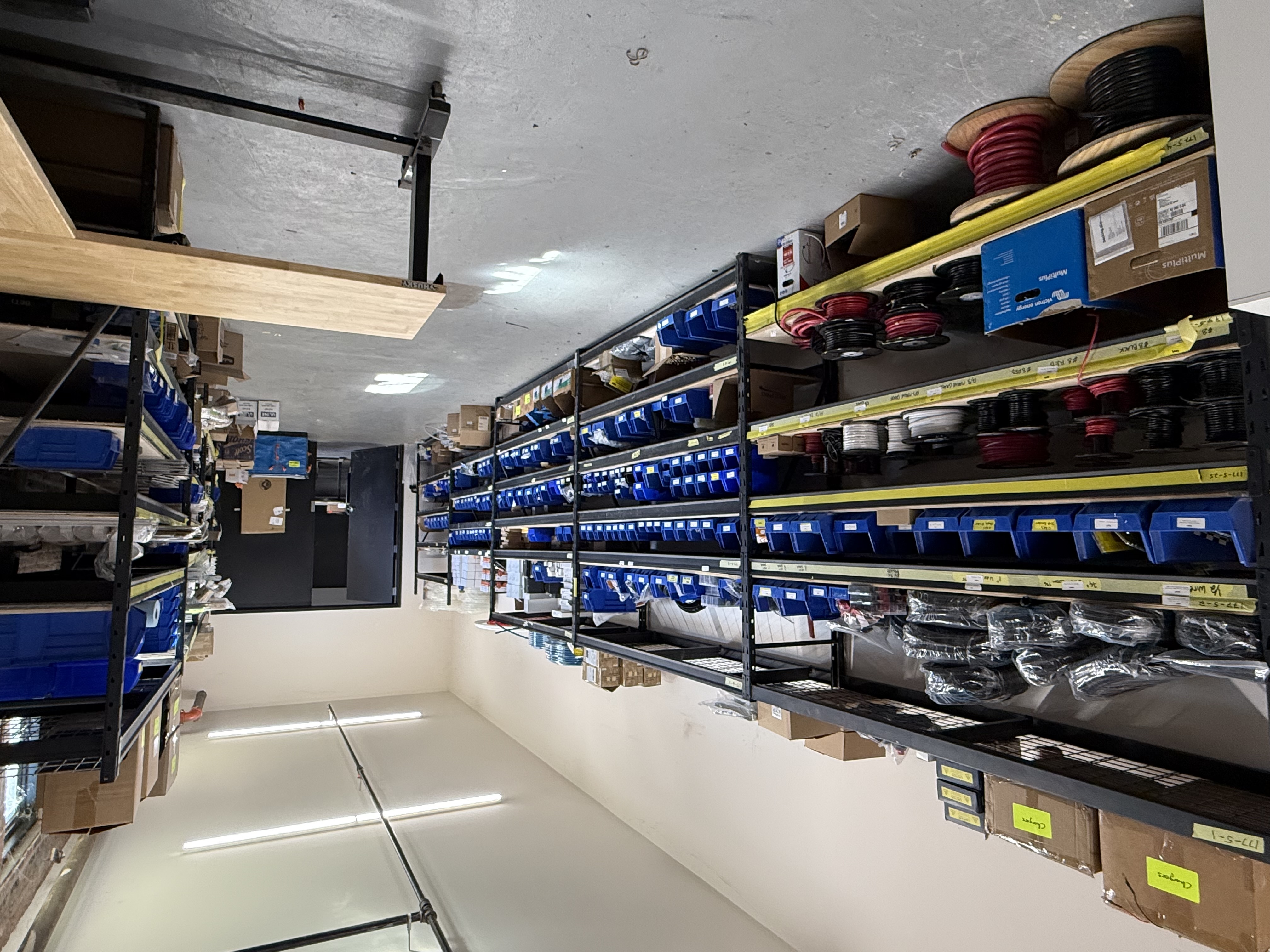 Supply room shelves stocked with labeled bins, wire, and build hardware.