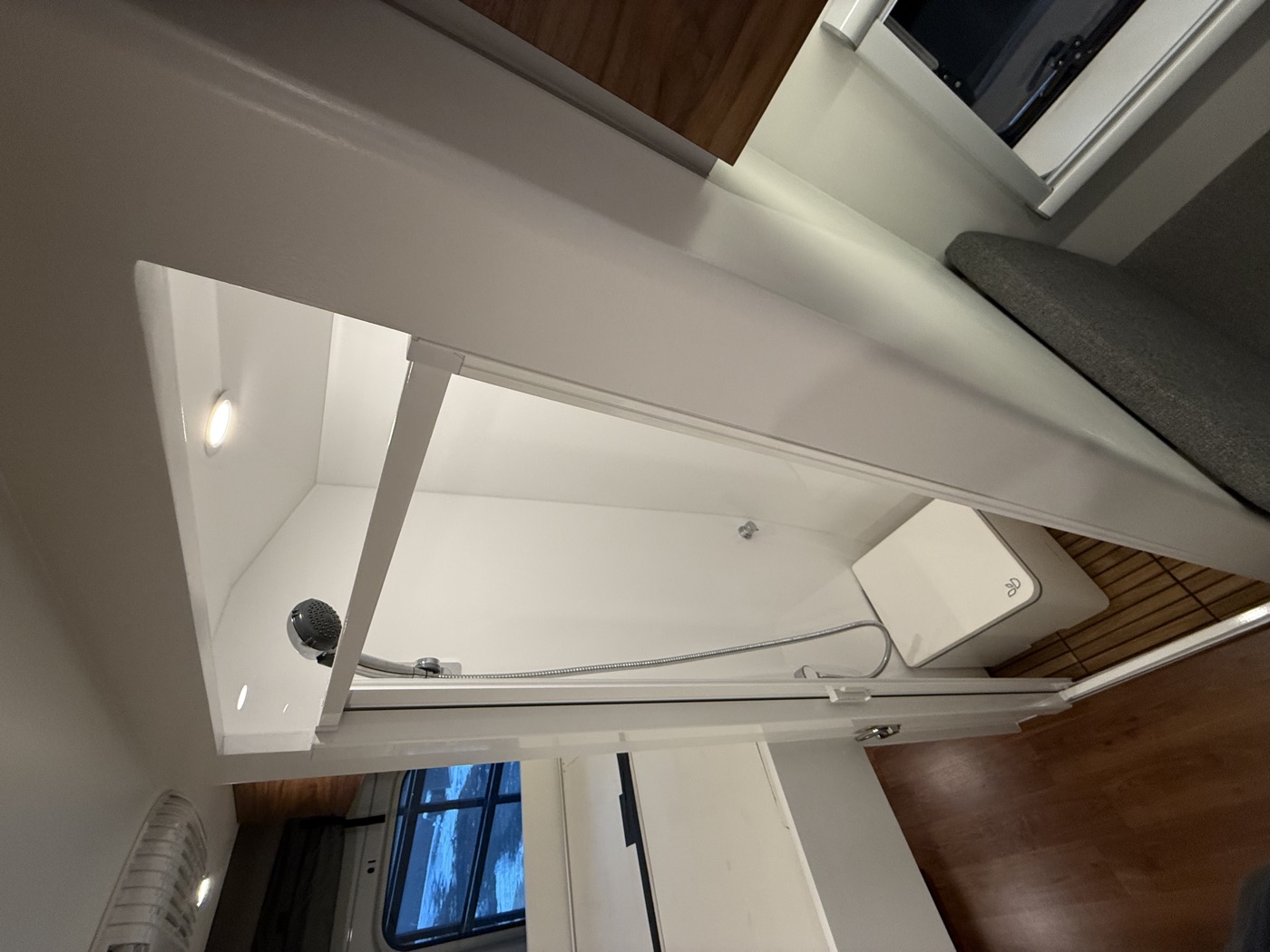 Completed van shower with white wall panels and teak floor insert.