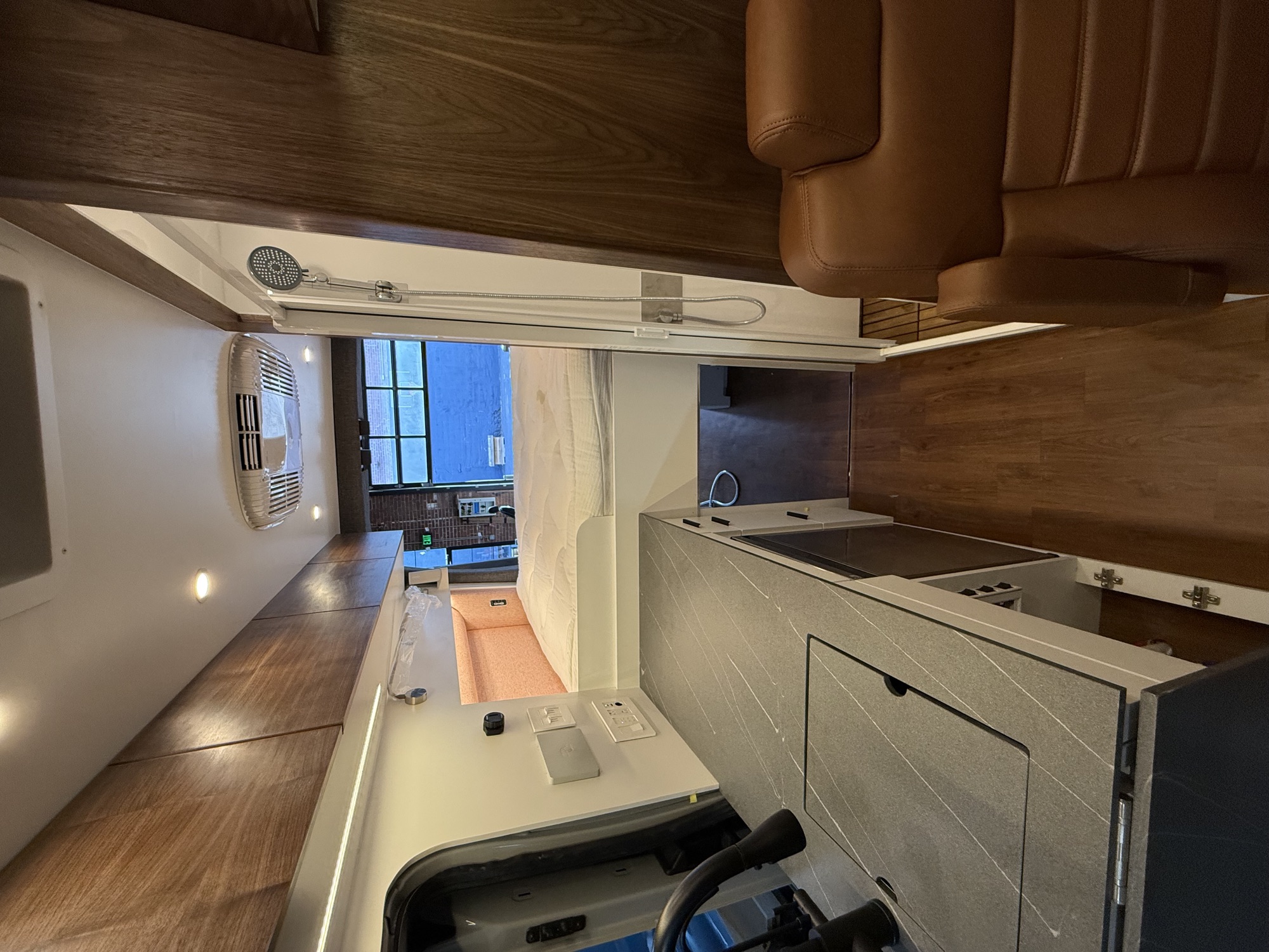 Finished van interior with cabinetry, galley, shower, and bed platform.